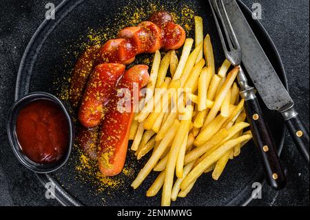 Currywurst tedesco tradizionale, servito con patatine fritte. Sfondo nero. Vista dall'alto Foto Stock