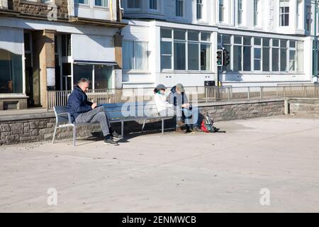 Penzance, Cornovaglia, 26 febbraio 2021, in una giornata gloriosa di sole persone distanza sociale da sedersi ad ogni estremità di una panchina durante il blocco a Penzance, Cornovaglia. La temperatura è 10C e si prevede di continuare per i prossimi giorni.Credit: Keith Larby/Alamy Live News Foto Stock