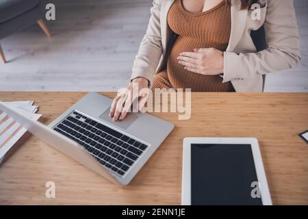 Foto ritratto ritagliata in alto sopra la vista ad angolo alto della gravidanza donna che lavora su un computer portatile alla scrivania in un ufficio moderno Foto Stock