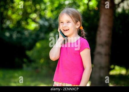 Felice allegra bambina, bambino che parla al telefono ridendo, ragazzino con uno smartphone, telefonata all'aperto, ritratto, spazio di copia Telecomunicazioni, Foto Stock