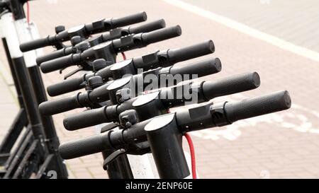 Scooter urbani moderni, numerosi scooter elettrici a noleggio in fila, manubrio in primo piano, dettaglio, parcheggio. Spostamenti ecologici giornalieri, altern semplice Foto Stock