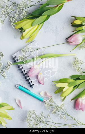 Spazio di lavoro con diario, taccuino, penna, fiori su sfondo azzurro. Scrivania da ufficio. Vista dall'alto sfondo femminile. Disposizione piatta, vista dall'alto. Foto Stock