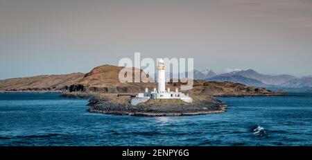 Vista sul vecchio Eilean Musdile faro in Scozia, con cime highland picchi in background Foto Stock