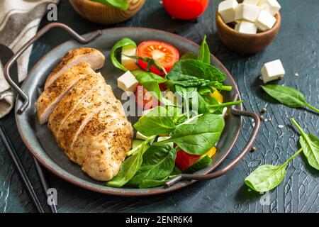 Cibo sano. Pranzo con dieta chetogenica. Filetto di pollo alla griglia con insalata di verdure fresche, spinaci e feta su fondo di pietra scuro. Foto Stock