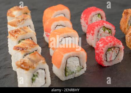 Set di deliziosi panini freschi di sushi su superficie nera Foto Stock