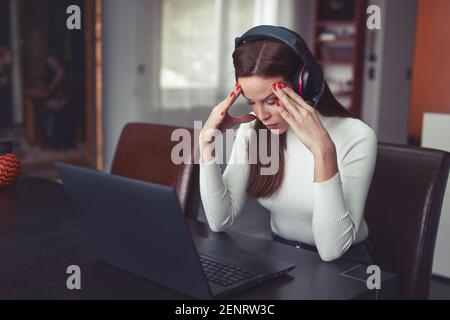 Giovane stanca, donna caucasica intelligente in cuffia ha mal di testa al computer portatile, in interni Foto Stock