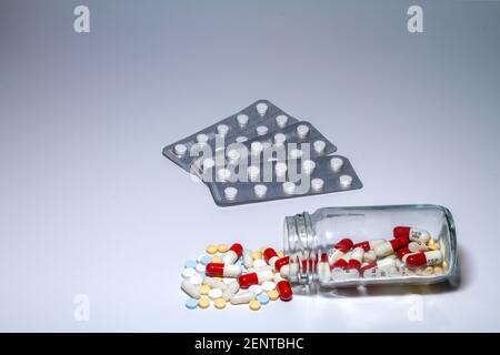 Confezione blister di pillole bianche accanto a un flacone di vetro trasparente che si trova dal punto in cui fuoriescono compresse e capsule di colore giallo, blu, rosso e bianco. Foto Stock