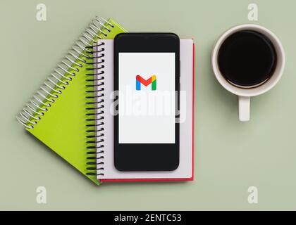 Logo Gmail sullo schermo nero dello smartphone con notebook e. tazza di caffè su sfondo verde Foto Stock