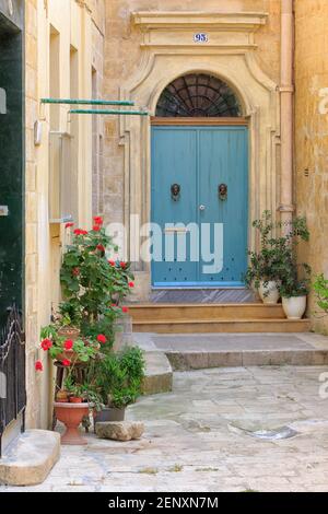 Strada stretta con una casa in pietra calcarea con un colorato balcone tradizionale chiuso in legno e porta con battitori leone in metallo a la Valletta, Malta Foto Stock