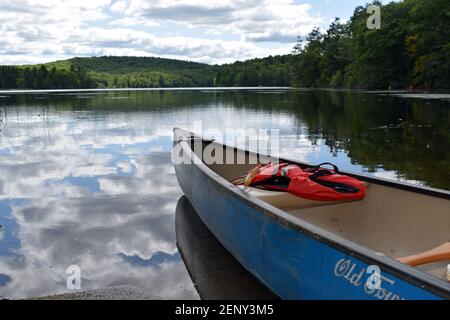 Una canoa si protende verso Burr Pond nel Connecticut, con le nuvole che si riflettono nell'acqua. Foto Stock