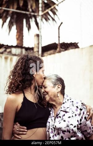 Giovane attraente donna messicana bacia sua nonna sulla strada estiva Foto Stock