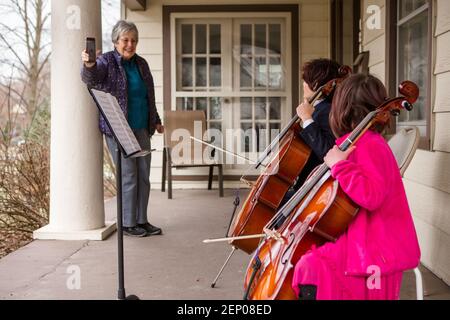 Una donna anziana registra due bambini che danno un concerto di violoncello portico Foto Stock