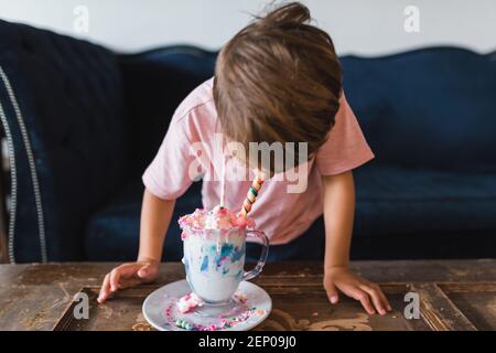 Ragazzo che beve un colorato frullato di latte davanti a un divano blu vintage. Foto Stock