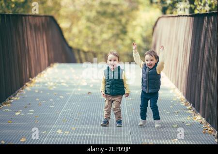 Due bambini super positivi che hanno due gemelli su un walk-in parco autunnale Foto Stock