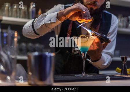 Il barista del bar rende la fiamma su un cocktail con buccia di arancia close up Foto Stock