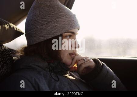 Una ragazza in abiti grigi guarda fuori il finestrino dell'auto, si appoggia sulla sua mano. Foto Stock