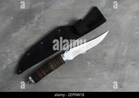 Un elegante coltello da caccia con scabarda e manico in pelle su fondo grigio cemento. Messa a fuoco selettiva. Foto Stock