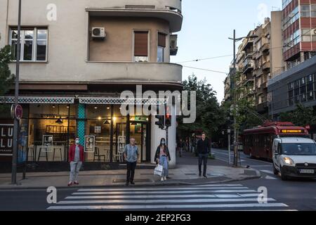 BELGRADO, SERBIA - 12 MAGGIO 2020: Uomo anziano e giovane uomo che cammina e guarda un traffico stradale su un viale di Belgrado indossare maschera prott Foto Stock