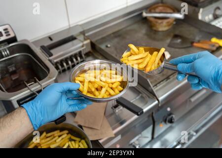 Primo piano sulle mani di uomo sconosciuto imprenditore con blu guanto protettivo in gomma che mette patatine fritte francesi in metallo piatto al fast food resto Foto Stock