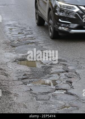 26 febbraio 2021, Brandeburgo, Francoforte (Oder): Un'automobile guida su una strada piena di buche. L'inverno non è ancora finito, ma il cambio di gelo e di rugiada finora ha probabilmente avuto un forte impatto sulle strade del Brandeburgo. Questo è il timore dell'agenzia statale per la circolazione stradale e dei comuni responsabili, ma non sono ancora in grado di redigere un bilancio dei danni. Foto: Patrick Pleul/dpa-Zentralbild/ZB Foto Stock