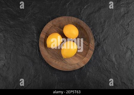 Piatto di legno di tre limoni freschi su superficie nera Foto Stock