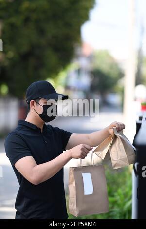 Corriere uomo in maschera protettiva consegnando il sacchetto ordine con porta del cibo. Foto Stock