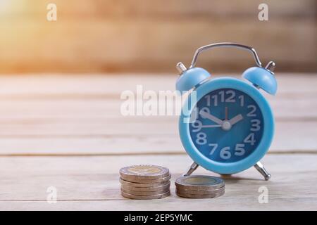 Monete, orologio alram e matita con notebook vuoto su sfondo tavola di legno. Scrivania da ufficio con monete e concetto di pianificazione finanziaria aziendale Foto Stock