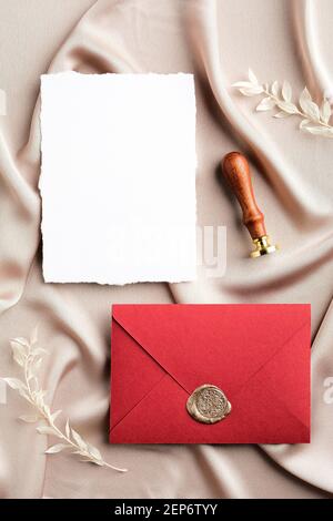Busta rossa con sigillo in cera e mockup di biglietti d'invito per matrimoni in bianco su tessuto satinato. Disposizione piatta, vista dall'alto, spazio per la copia. Set di cancelleria per matrimoni. Foto Stock