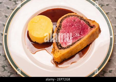 Fetta di filetto di Wellington di manzo con sugo di vino rosso E purè di patate su un piatto Foto Stock