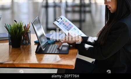 Ripresa di una giovane designer femminile o graphic designer che lavora con un computer tablet su una scrivania in legno per ufficio. Foto Stock