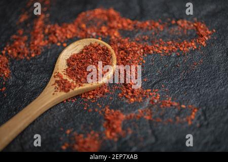 Cucchiaio di legno con peperoncino rosso caldo su pietra nera sfondo Foto Stock