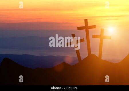 Gesù Cristo croce su uno sfondo con cielo drammatico, illuminazione, rosso colorato, tramonto arancione, nuvole scure, raggi solari, raggi solari che si illuminano dietro i tre Foto Stock