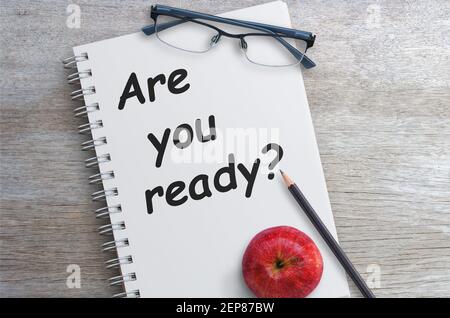 Domanda sei pronto sulla pagina del notebook con matita e mele rosse su un tavolo di legno nell'area di lavoro dell'ufficio. Foto Stock