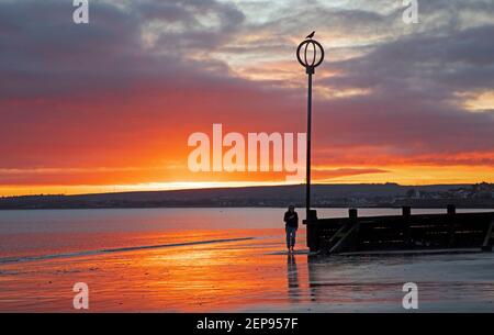 Portobello, Edimburgo, Scozia. Meteo nel Regno Unito. 27 febbraio 2021. Spettacolare alba sul mare Firth of Forth. In questo ultimo fine settimana d'inverno la temperatura è di 5 gradi C. goduto da questo camminatore. Foto Stock