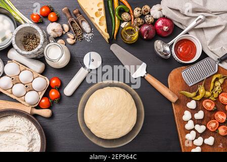 Pizza classica margherita con formaggio a forma di cuore. Preparazione di una cena di gala a fasi per due a casa in onore del giorno di San Valentino. Foto Stock