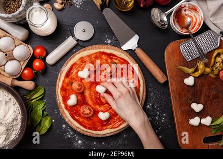 Pizza classica margherita con formaggio a forma di cuore. Preparazione di una cena di gala a fasi per due a casa in onore del giorno di San Valentino. Foto Stock