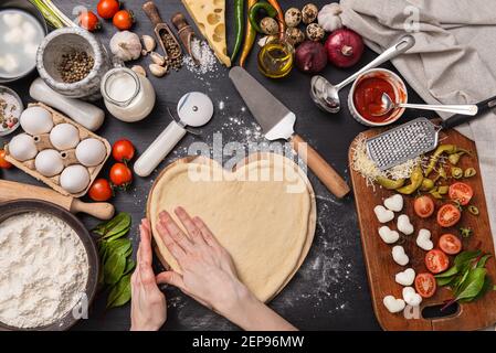 donna che prepara una cena festiva per due in onore di San Valentino classica pizza italiana Margherita a forma di un cuore e mozzarella nella cenere Foto Stock