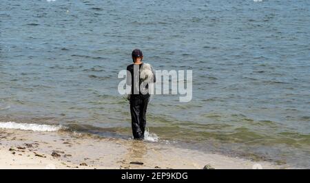 Pescatore che cammina su una spiaggia che porta una rete sulla sua spalla Foto Stock