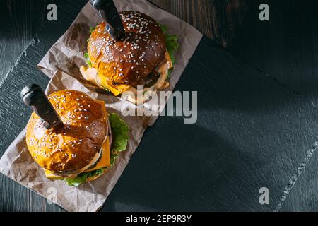 Due succulenti, deliziosi hamburger fatti in casa utilizzati per tritare il manzo. Sul tavolo di legno. Gli hamburger sono coltelli inseriti. Foto Stock