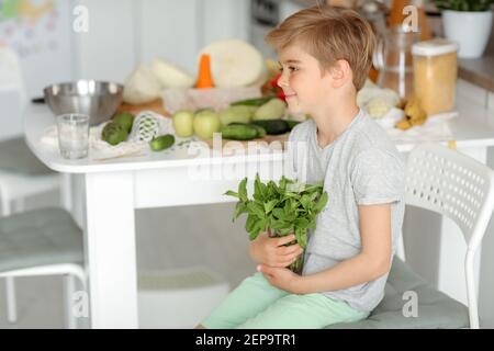 Il bambino mette le verdure sul tavolo e prepara un'insalata. Foto Stock