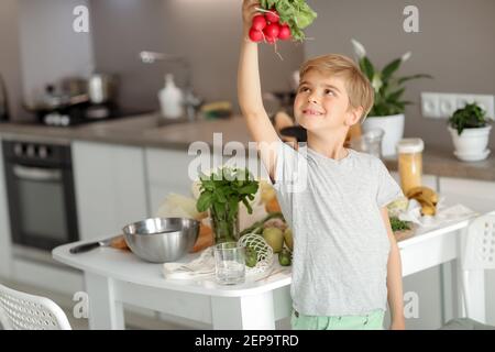 Il bambino mette le verdure sul tavolo e prepara un'insalata. Foto Stock