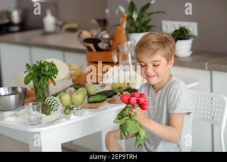Il bambino mette le verdure sul tavolo e prepara un'insalata. Foto Stock