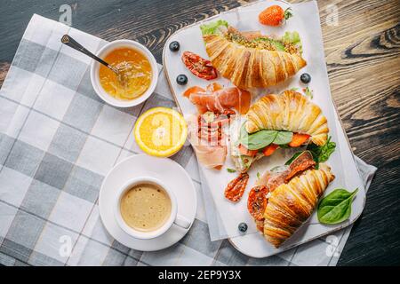 Il concetto di una ricca e gustosa colazione di croissant classici freschi con una varietà di condimenti da ricotta jamon avocado, fragole, essiccati al sole Foto Stock