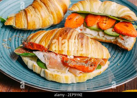 Il concetto di una ricca e gustosa colazione di croissant classici freschi con una varietà di condimenti da ricotta jamon avocado, fragole, essiccati al sole Foto Stock