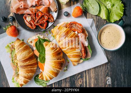 Il concetto di una ricca e gustosa colazione di croissant classici freschi con una varietà di condimenti da ricotta jamon avocado, fragole, essiccati al sole Foto Stock