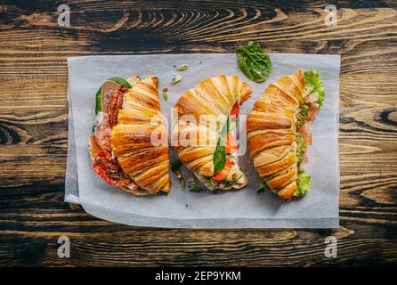 Il concetto di una ricca e gustosa colazione di croissant classici freschi con una varietà di condimenti da ricotta jamon avocado, fragole, essiccati al sole Foto Stock