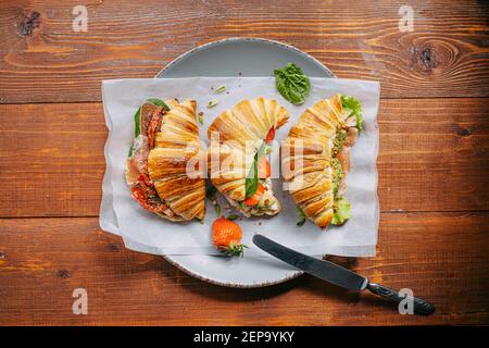 Il concetto di una ricca e gustosa colazione di croissant classici freschi con una varietà di condimenti da ricotta jamon avocado, fragole, essiccati al sole Foto Stock