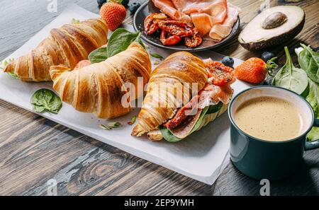 Il concetto di una ricca e gustosa colazione di croissant classici freschi con una varietà di condimenti da ricotta jamon avocado, fragole, essiccati al sole Foto Stock