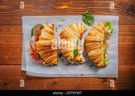 Il concetto di una ricca e gustosa colazione di croissant classici freschi con una varietà di condimenti da ricotta jamon avocado, fragole, essiccati al sole Foto Stock