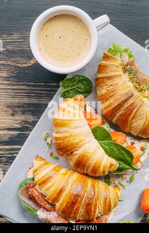 Il concetto di una ricca e gustosa colazione di croissant classici freschi con una varietà di condimenti da ricotta jamon avocado, fragole, essiccati al sole Foto Stock